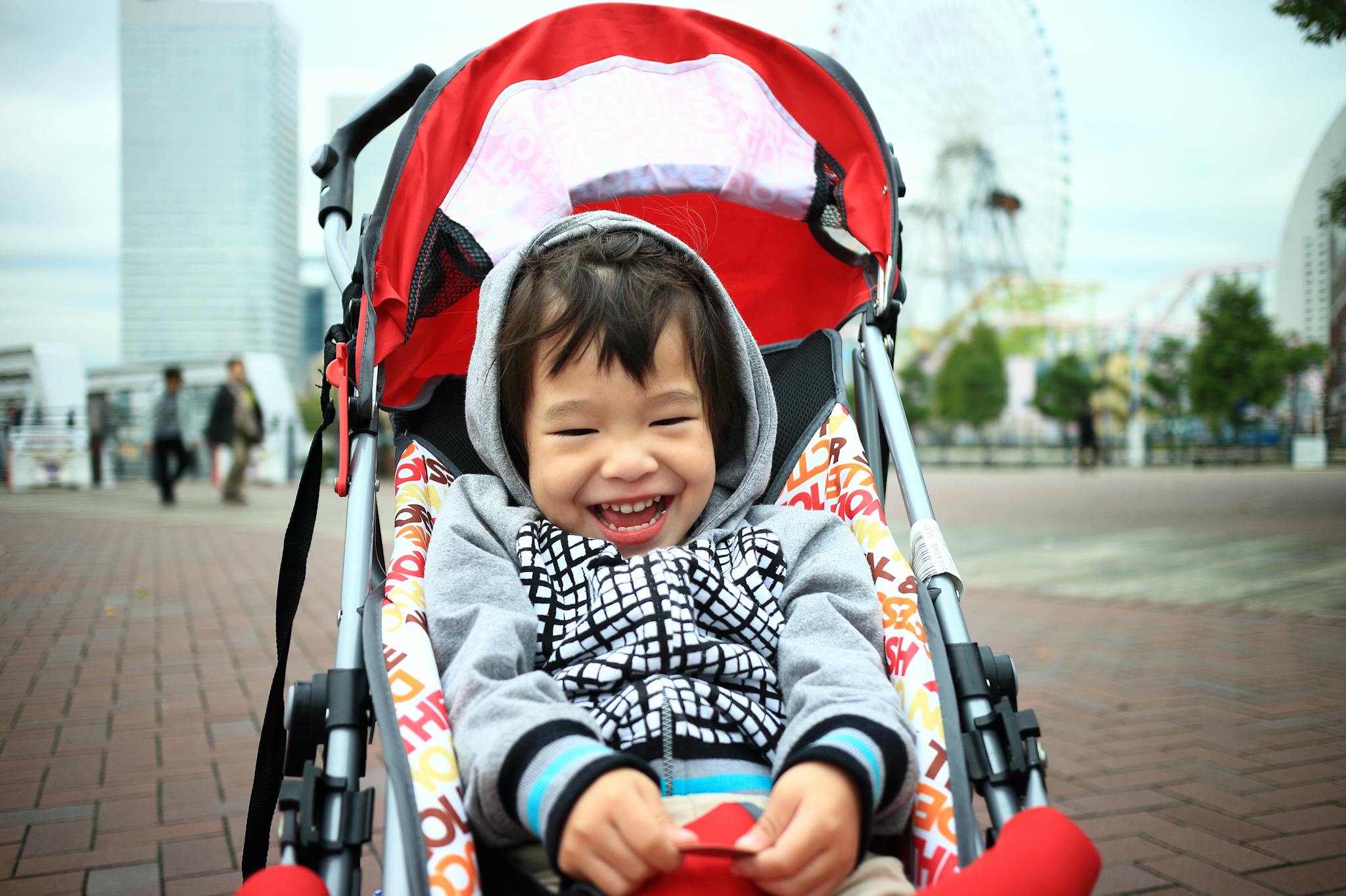 Smiling child sitting in a stroller enjoying a day out in Yokohama's urban park.
